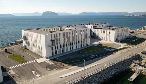 Hammerfest sykehus sett fra dronevinkel som viser bygget foran havet og parkeringsplass i front