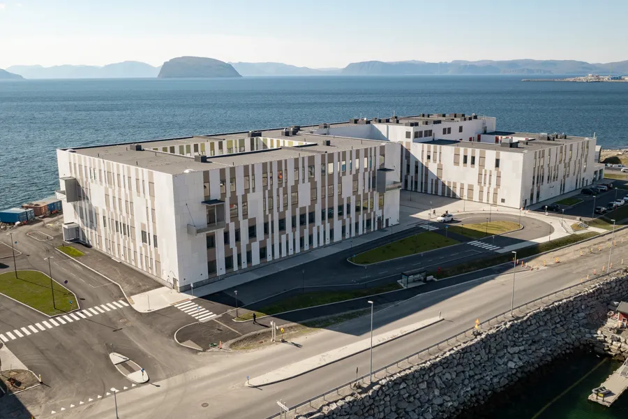 Hammerfest sykehus sett fra dronevinkel som viser bygget foran havet og parkeringsplass i front