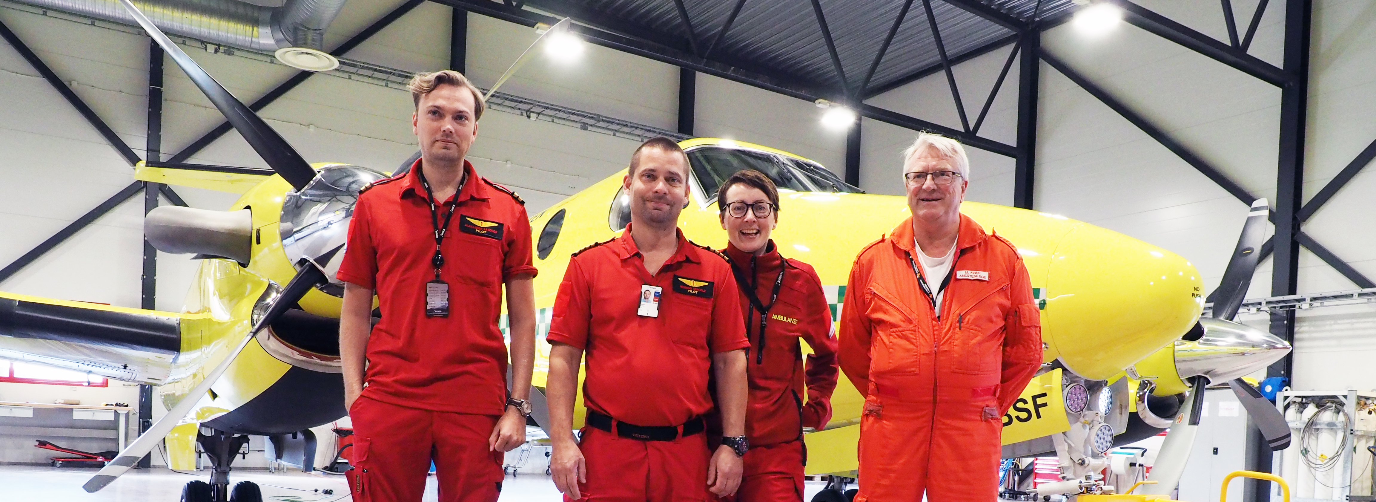 Ansatte foran ambulansefly inne i hangaren