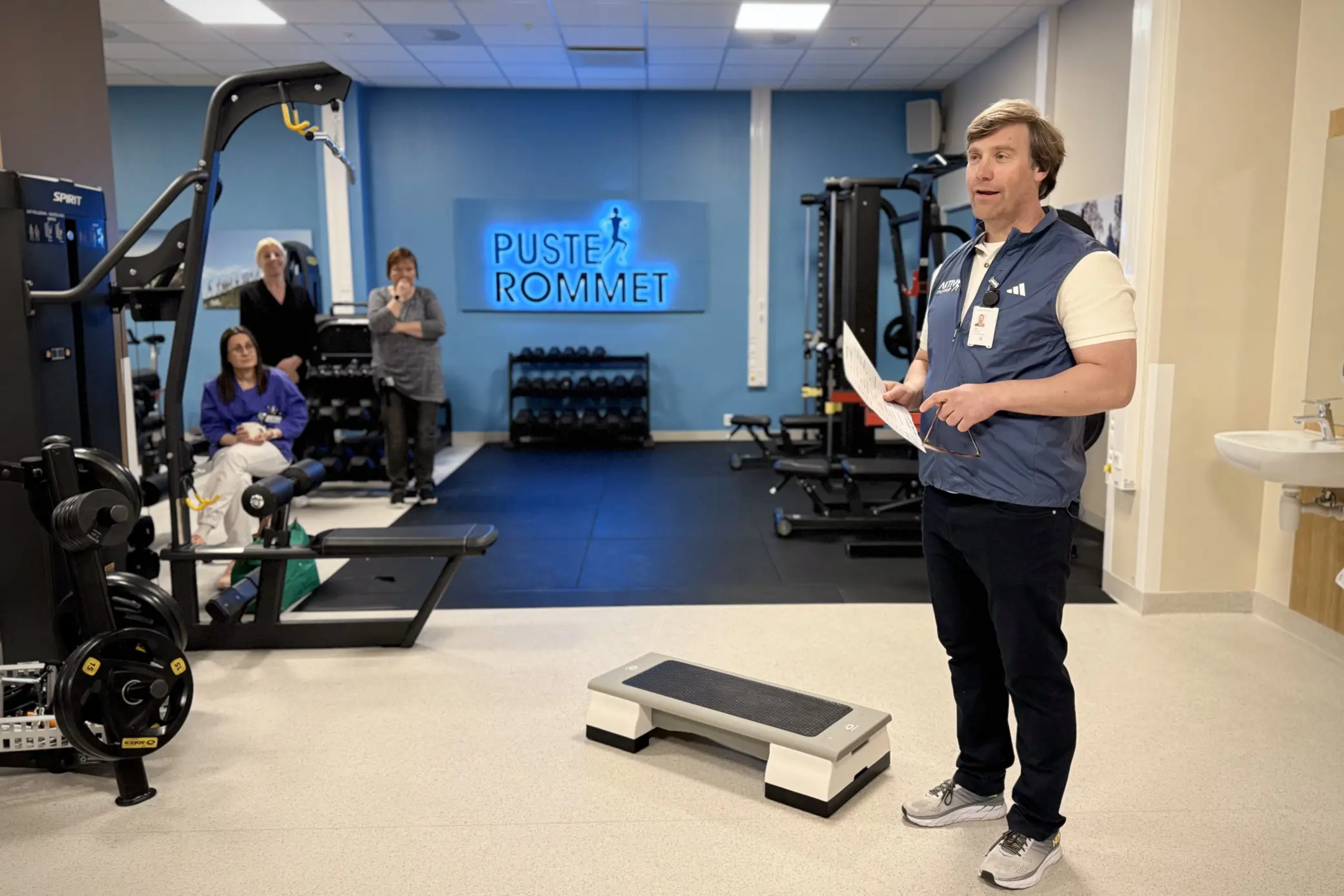 En person som står i et rom med treningsutstyr og mennesker i bakgrunnen