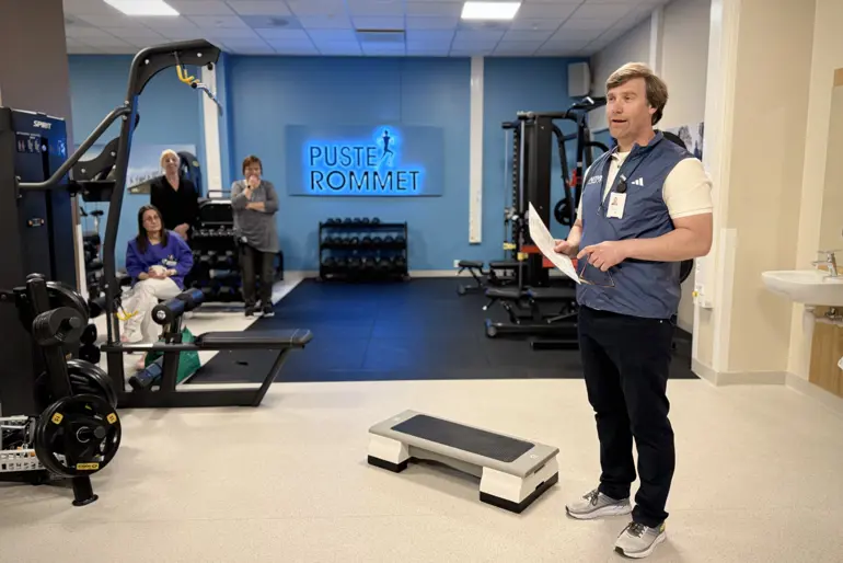 En person som står i et rom med treningsutstyr og mennesker i bakgrunnen