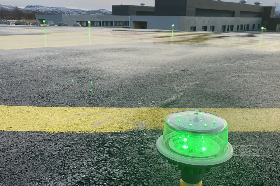 En grønn plastkopp på en gul stolpe foran en bygning